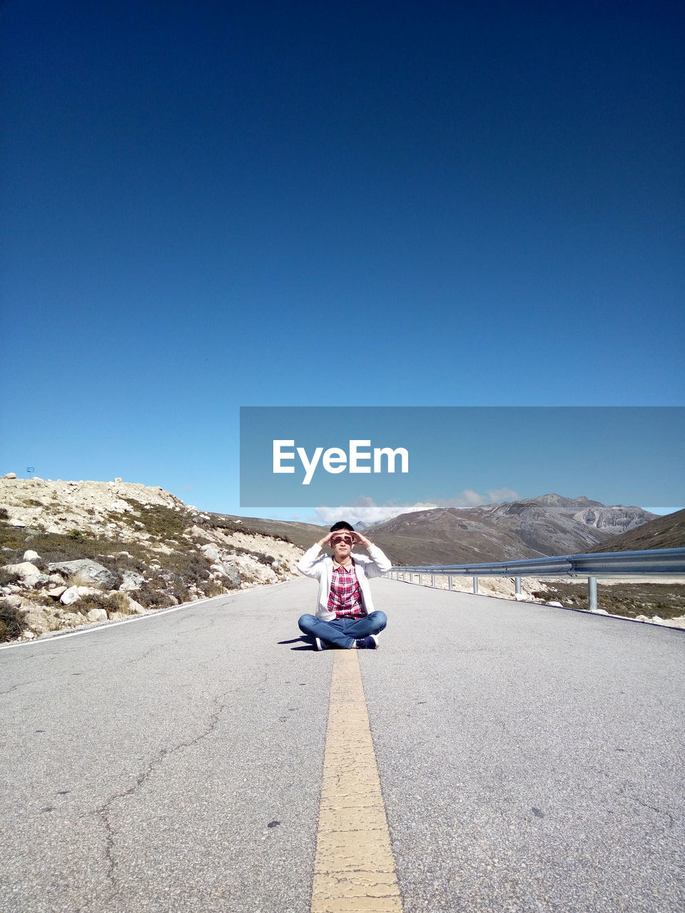 Man sitting on road against blue sky