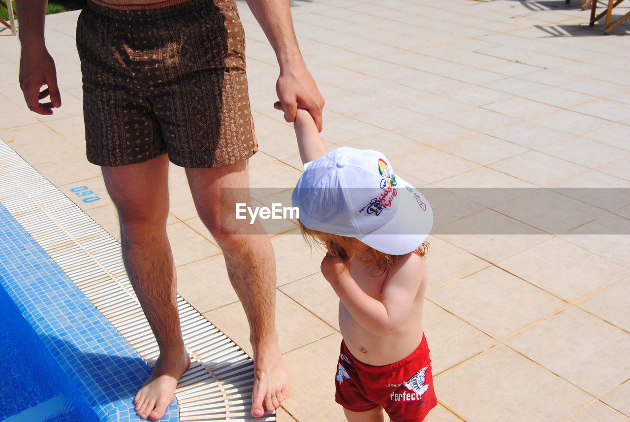 Low section of father with son standing at poolside