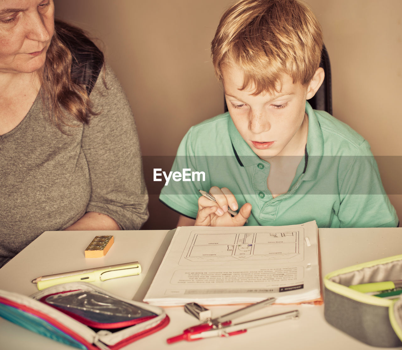 Mother teaching son while sitting by table at home