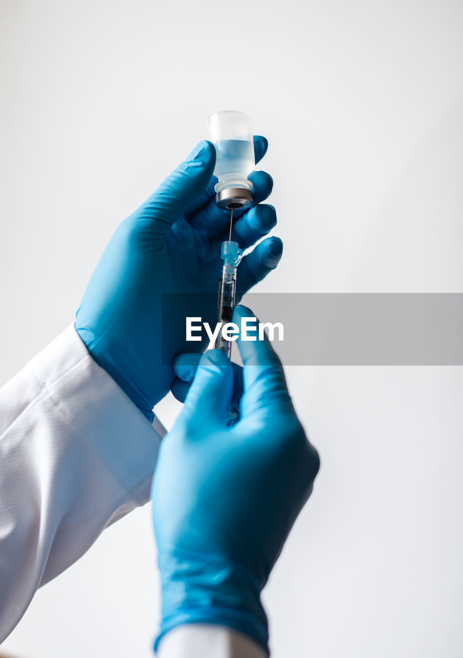 Hands in gloves drawing vaccine into syringe on white background.