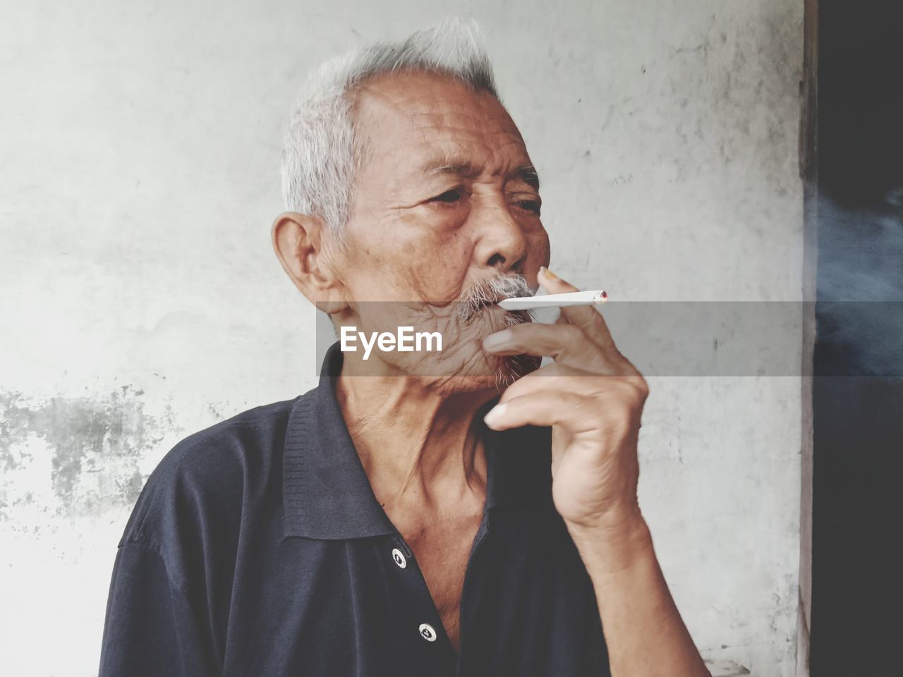 Senior man smoking cigarette against wall