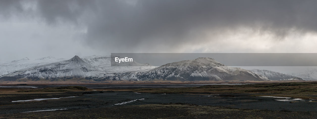 Scenic panoramic view of snow covered mountain range with ominous low hanging clouds