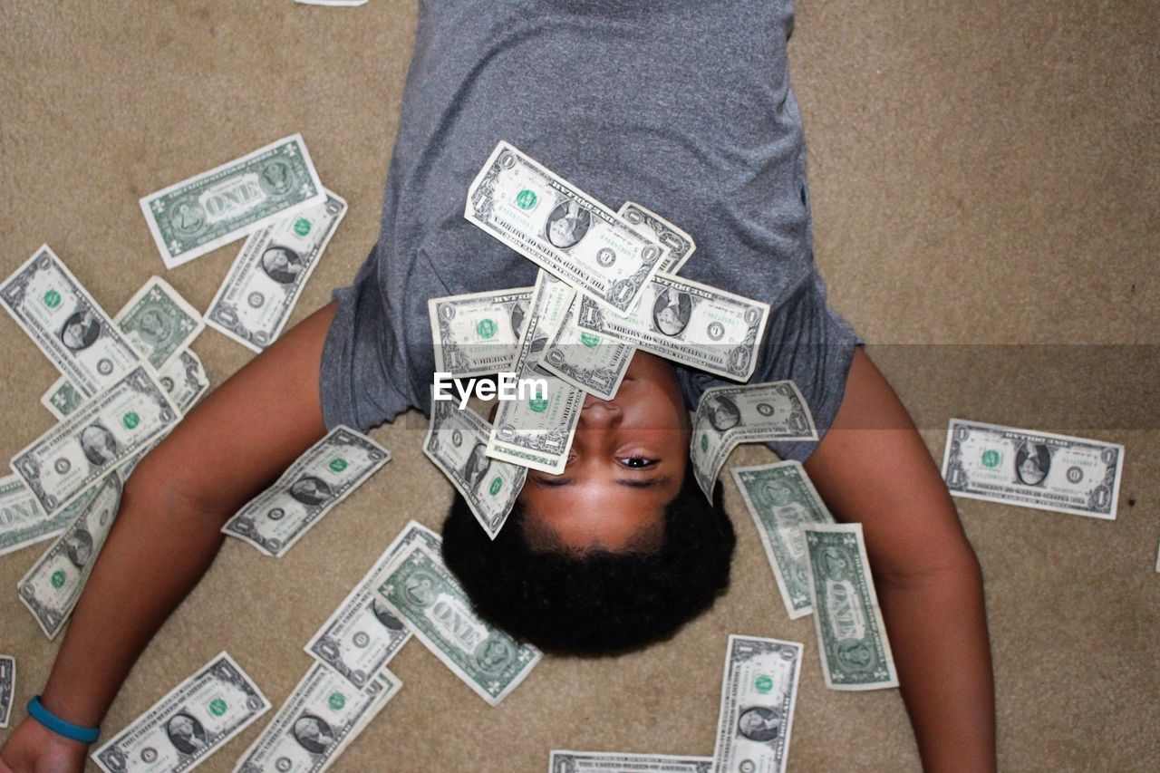 High angle portrait of boy surrounded by money while lying on floor