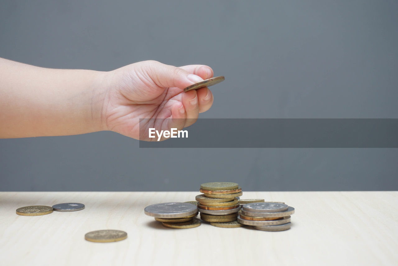 Close-up of hand holding coin over stack on table