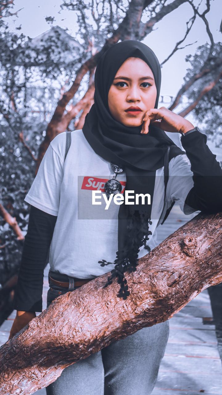 PORTRAIT OF WOMAN STANDING AGAINST TREE