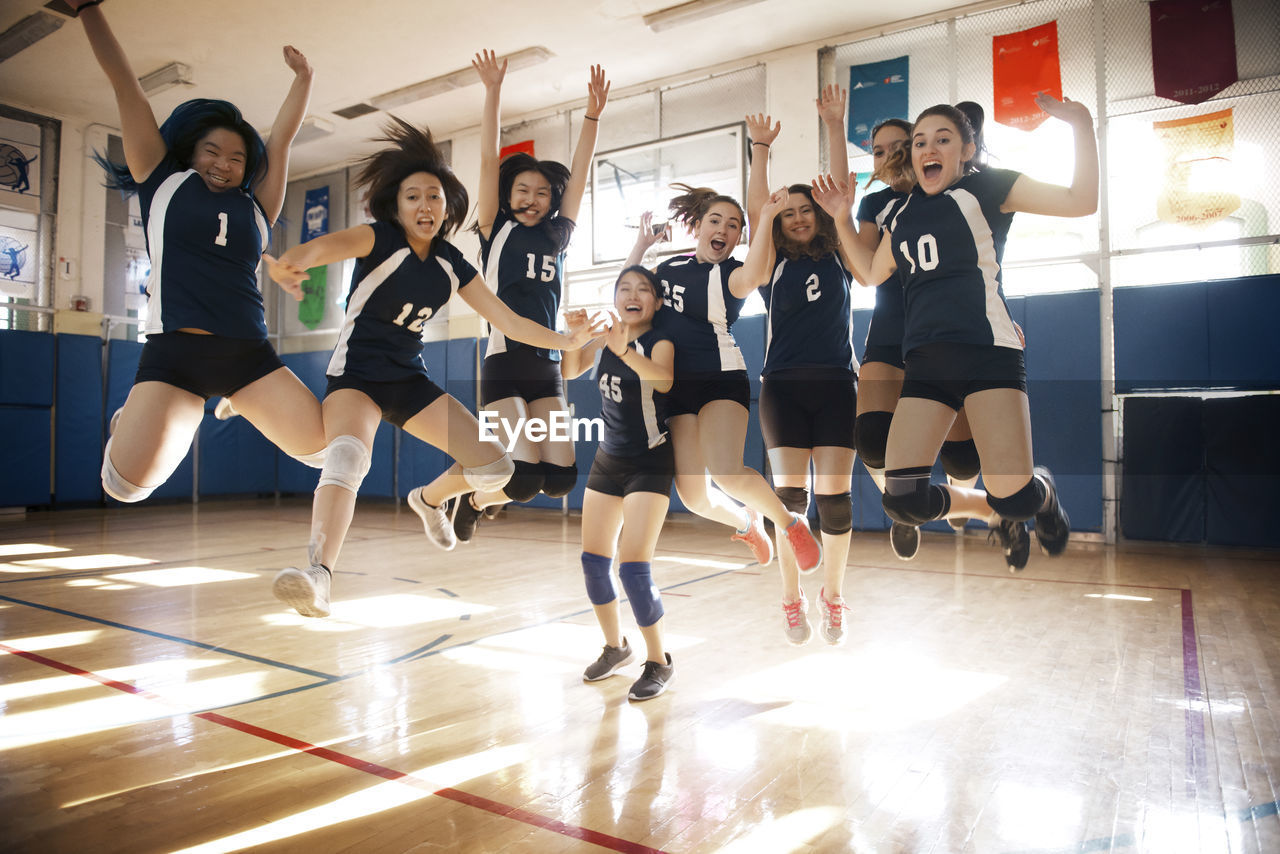 Happy female volleyball team jumping at court