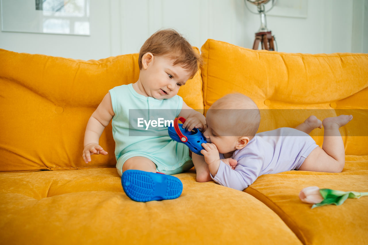 Two babies playing on a yellow sofa