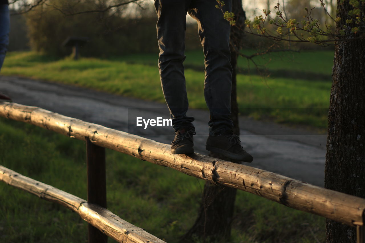 Low section of man standing on wooden railing at park