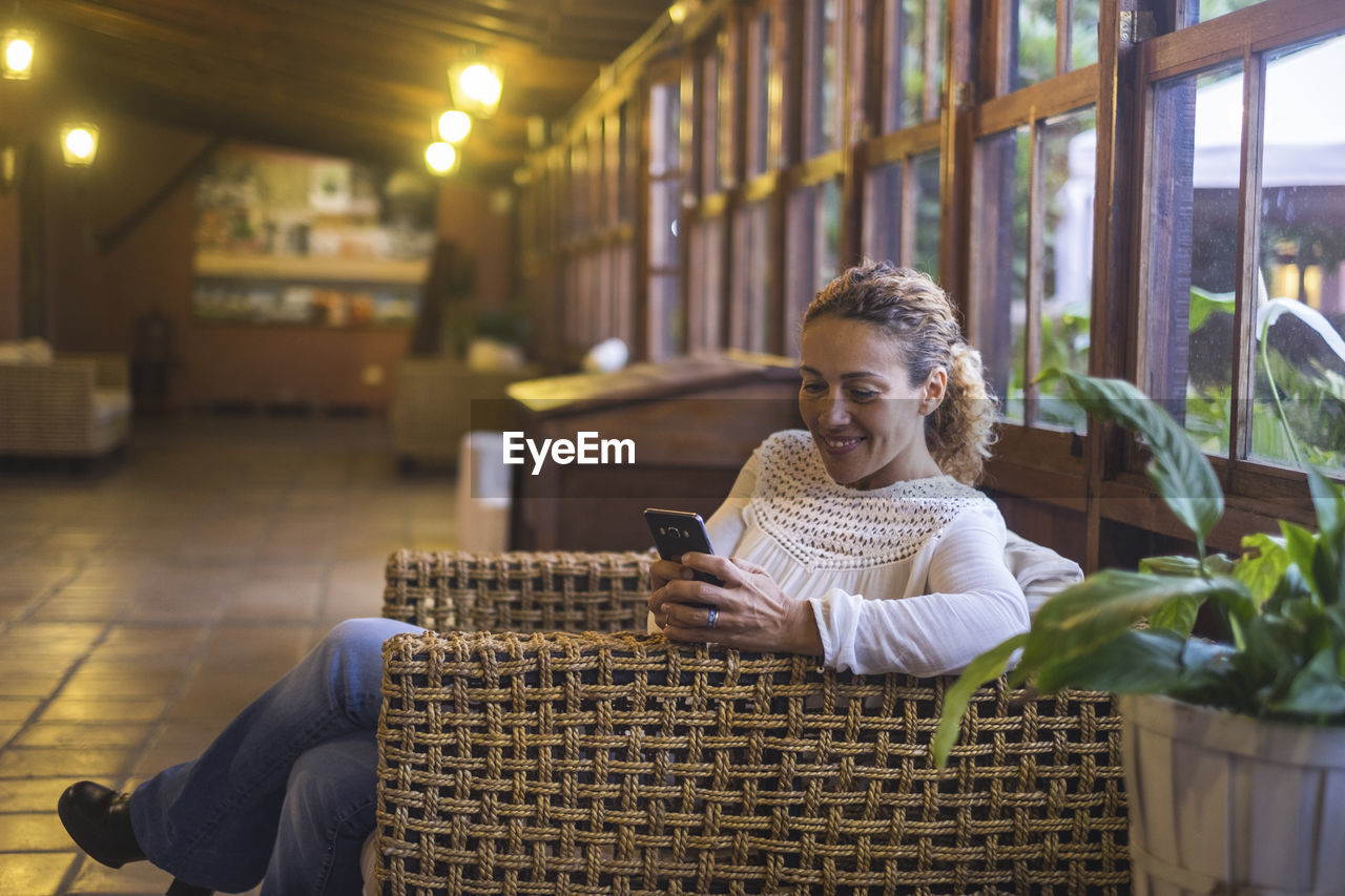 Smiling mature woman using mobile phone while sitting on sofa at home