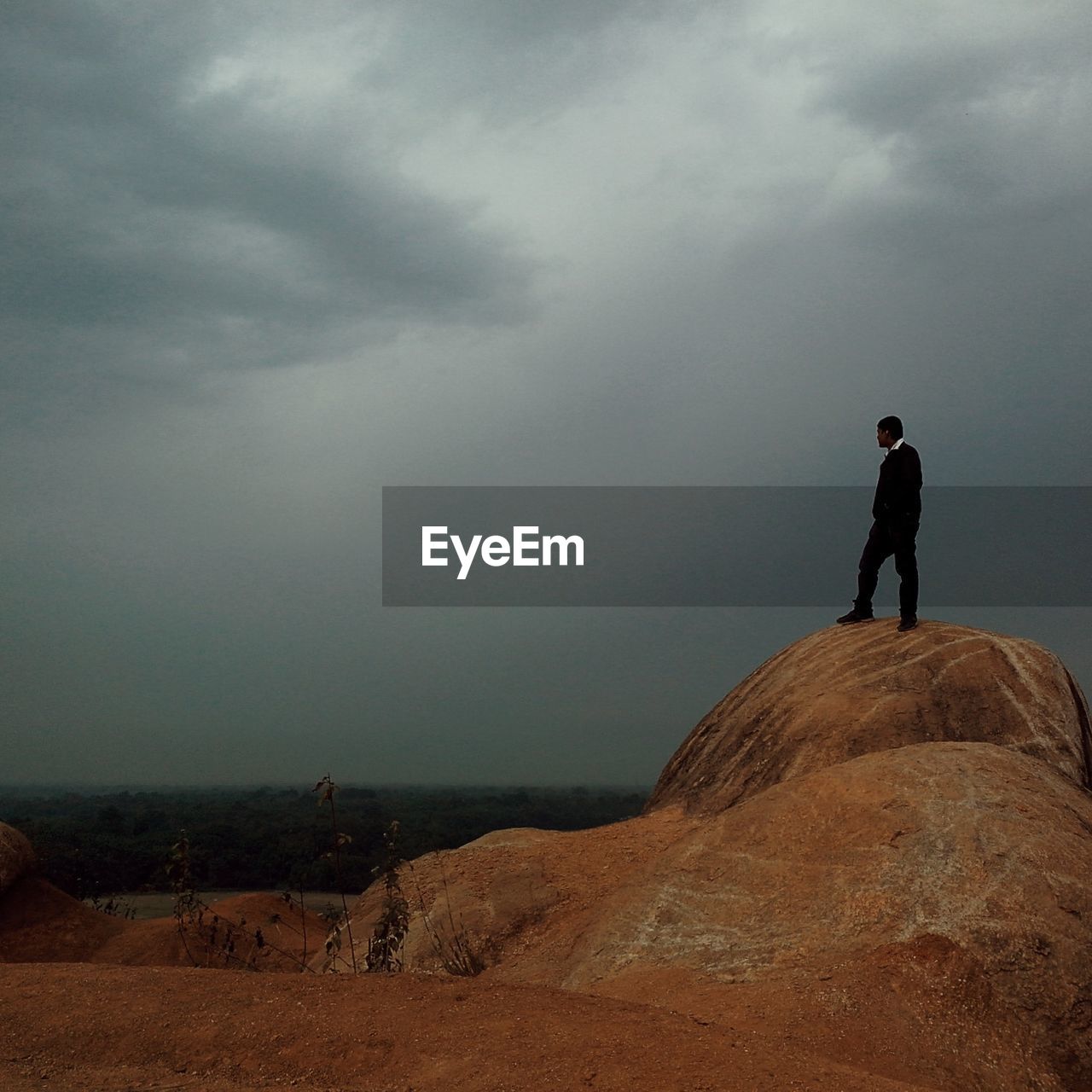 Low angle view of man standing on rock by sea against cloudy sky at dusk