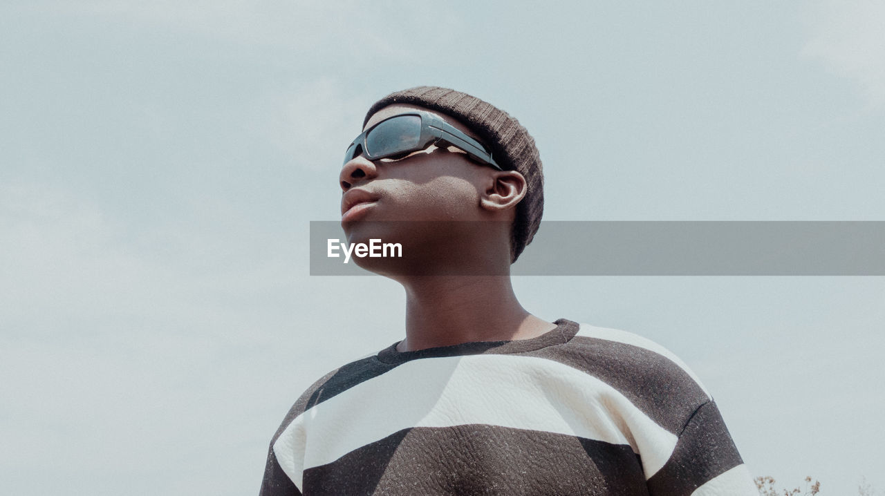 Low angle view of young man wearing sunglasses against sky