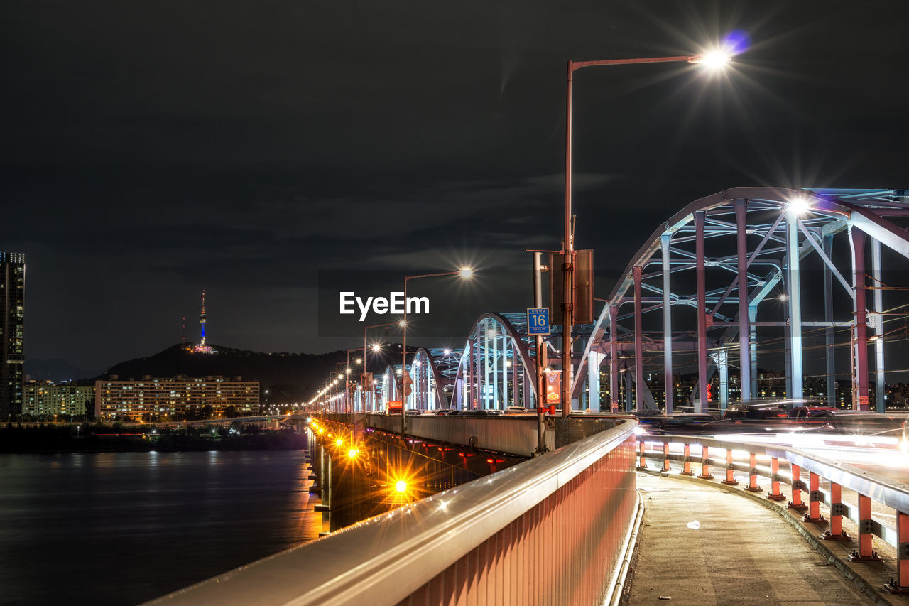 Illuminated bridge over river against buildings at night