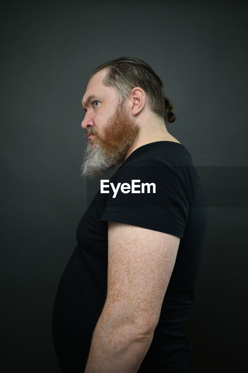 SIDE VIEW OF MAN LOOKING AWAY AGAINST BLACK BACKGROUND