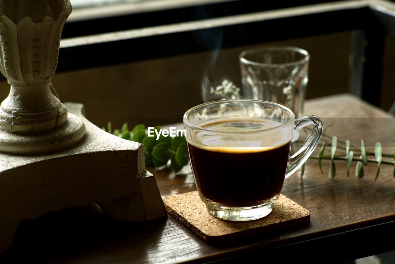 Glass of hot black coffee with smoke on the wooden desk