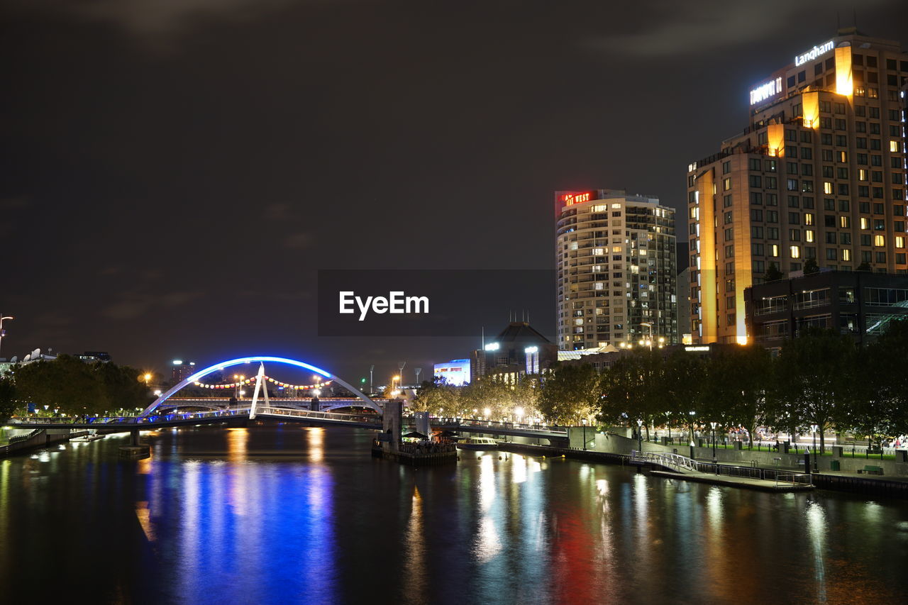 ILLUMINATED CITYSCAPE BY RIVER AGAINST SKY