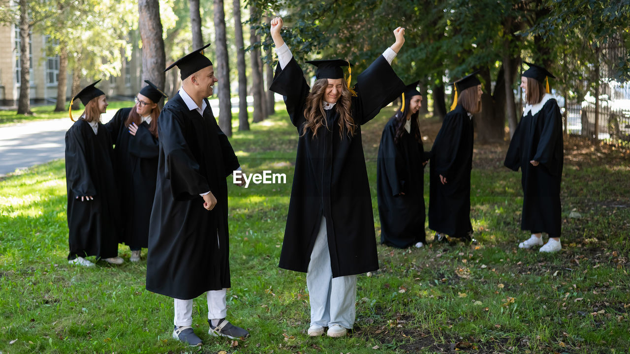 rear view of woman wearing graduation gown walking in traditional clothing standing in park