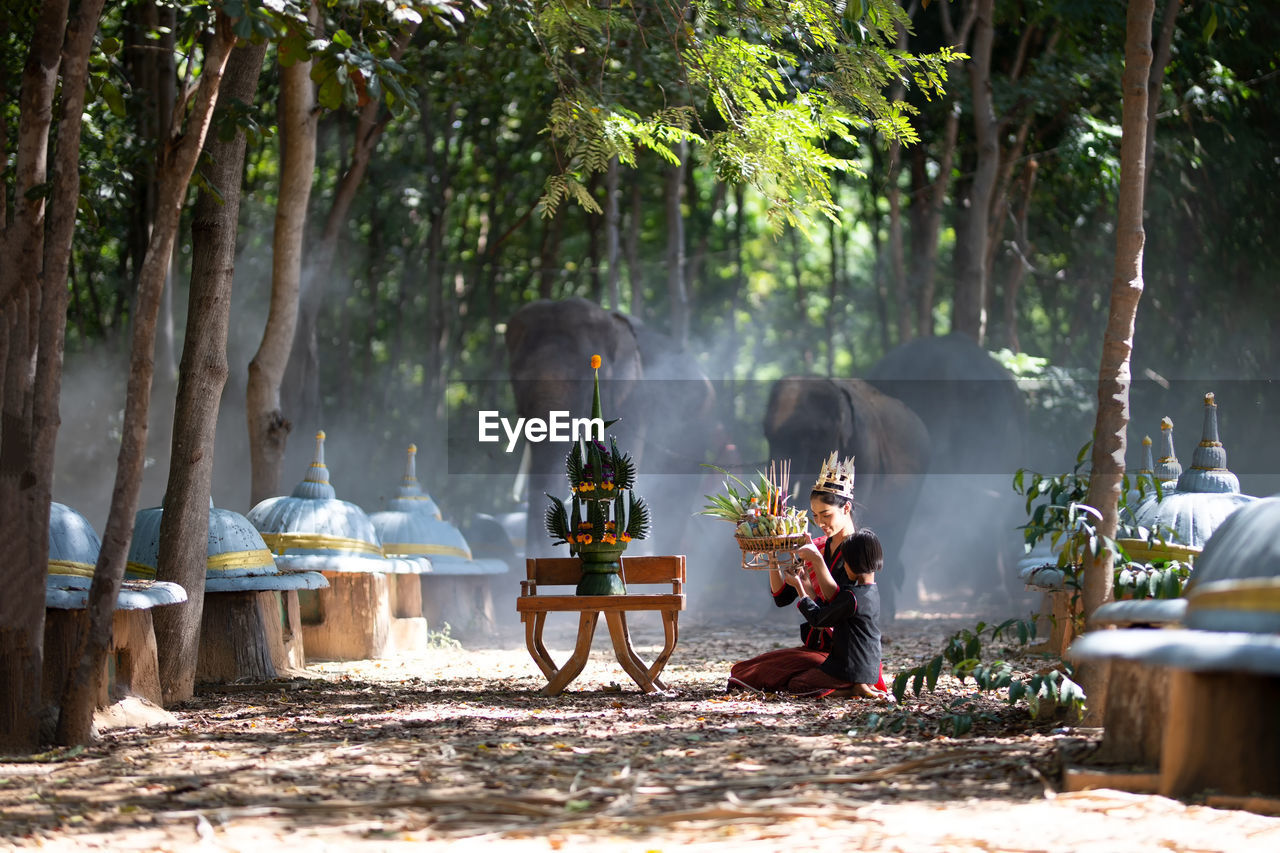 Woman with girl praying while sitting in forest