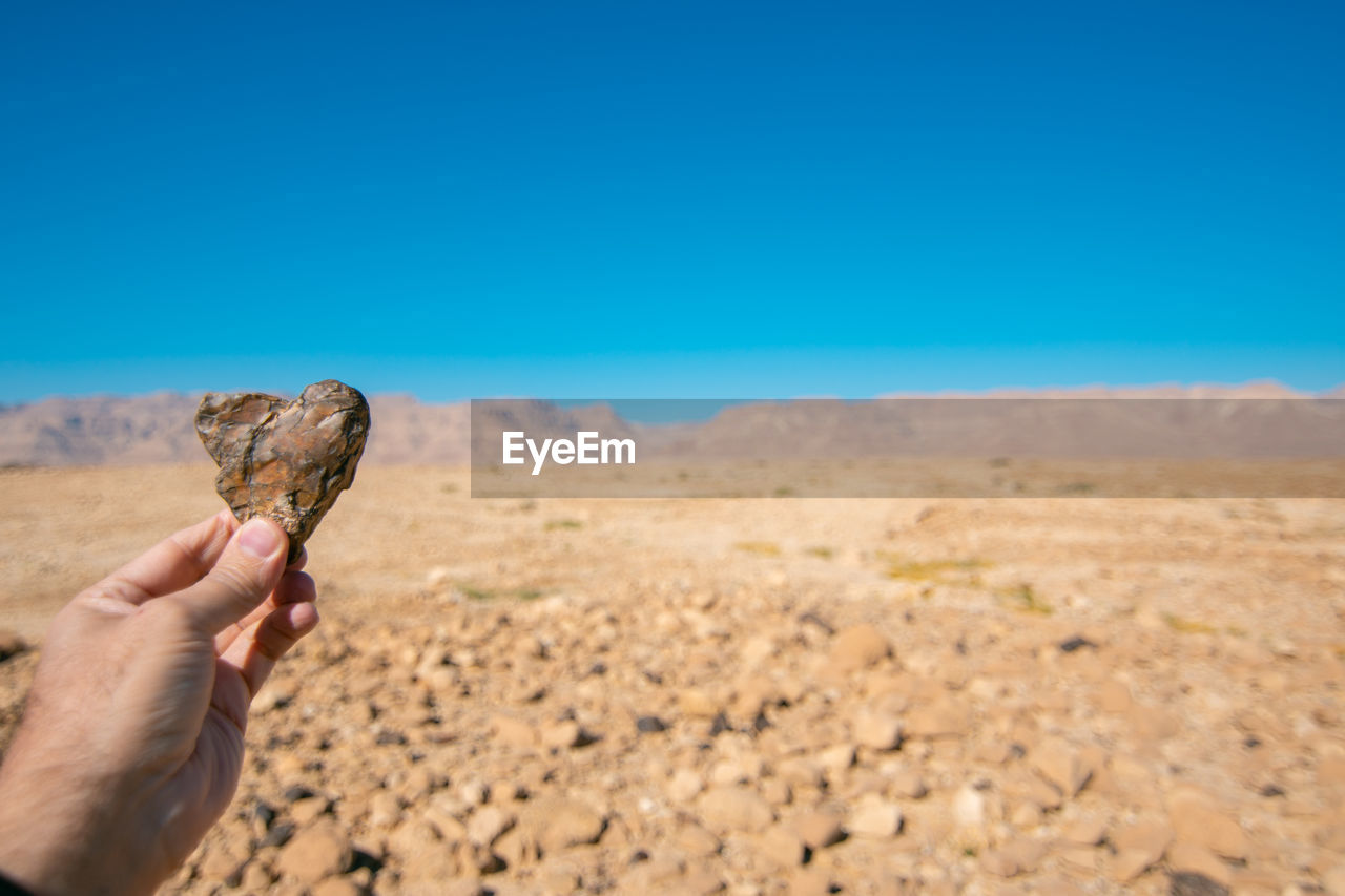 Person hand holding heart shape stone against clear sky