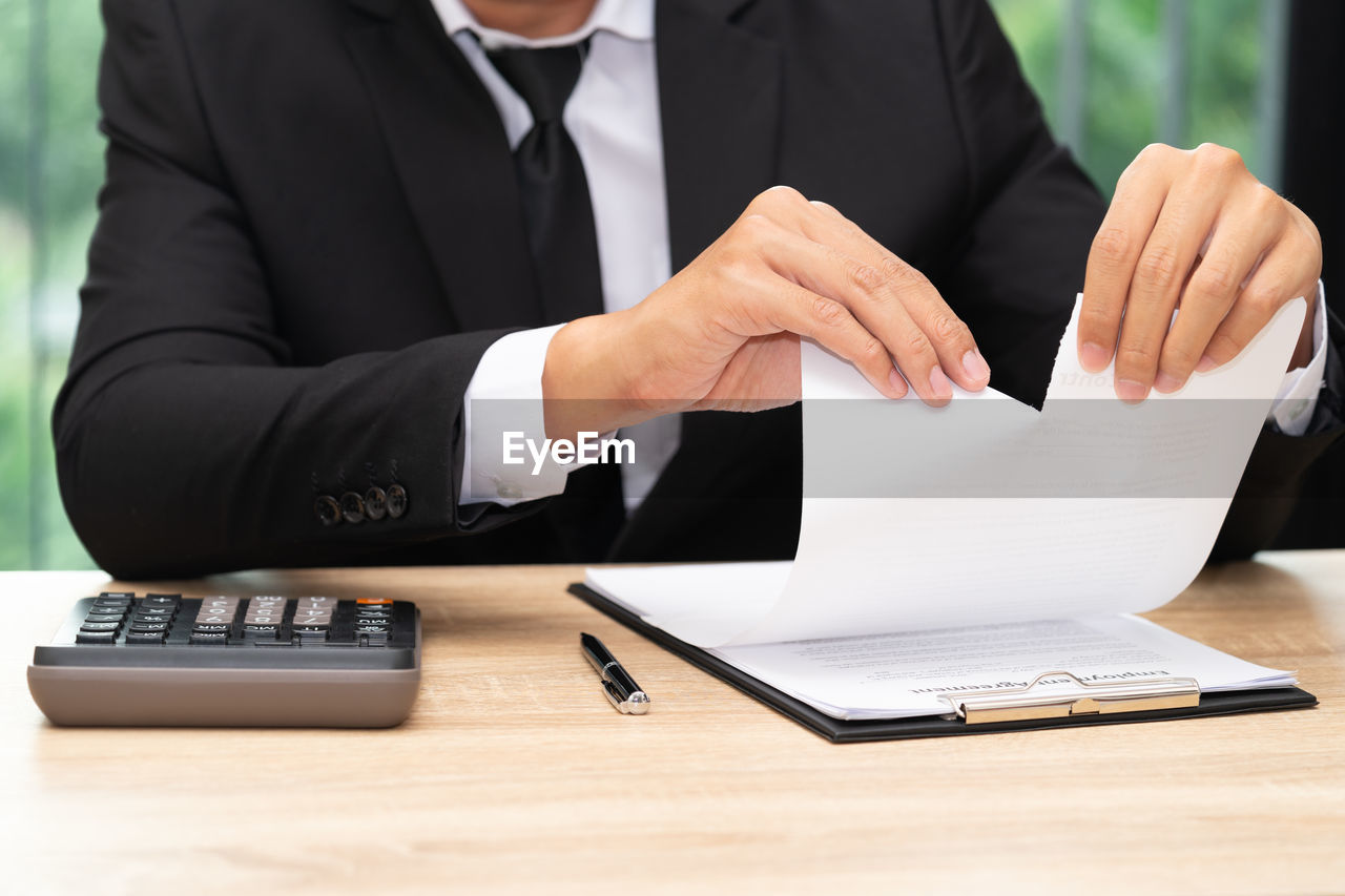 Midsection of businessman tearing document in office