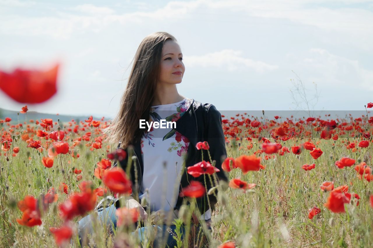 Woman standing by red poppy flowers in field