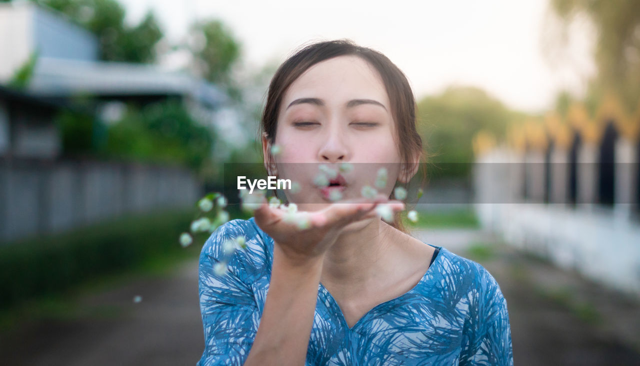 Young woman with eyes closed blowing flowers in hand 