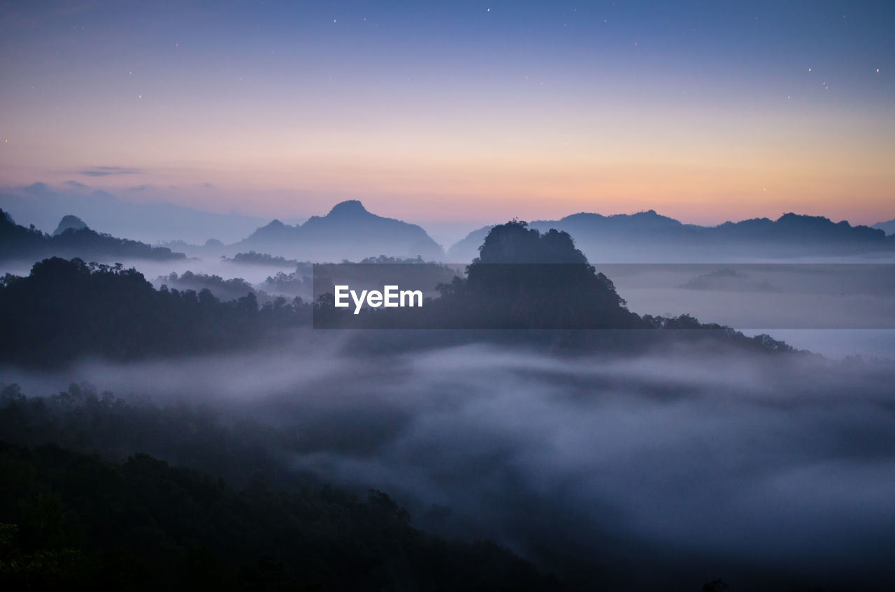 Scenic view of silhouette mountains in foggy weather during sunrise