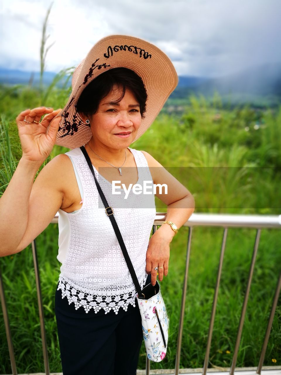 Portrait of woman in hat standing by railing against plants