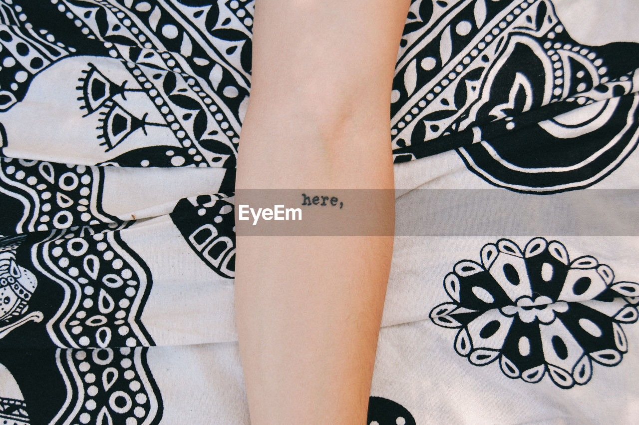 Cropped image of arm with tattoo on bed sheet