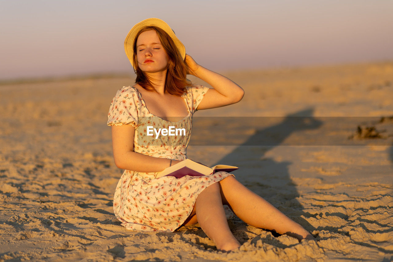 portrait of young woman standing on sand at beach