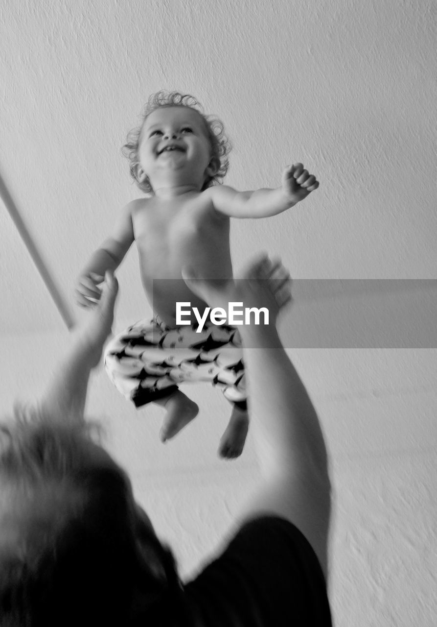 Low angle view of playful father catching baby boy in mid-air at home