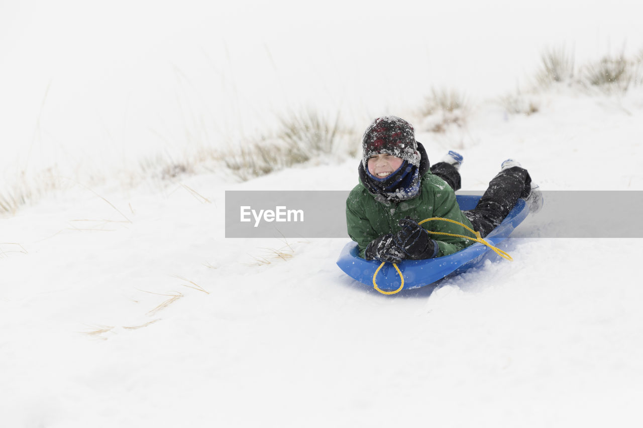 Teenage boy sledding on snow covered landscape during winter