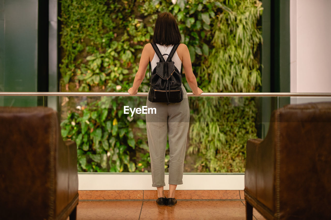 Full length rear view of young woman standing at window in hotel