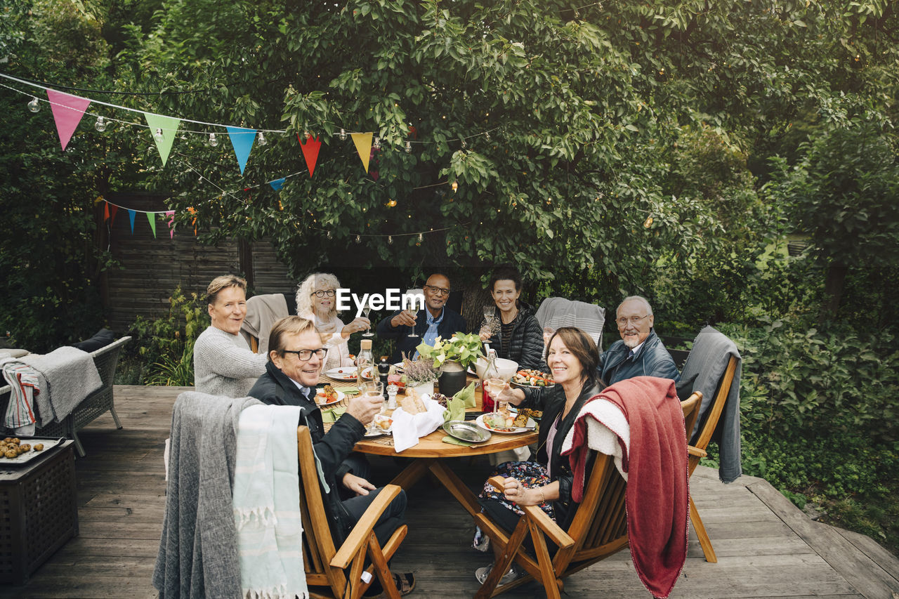 Portrait of smiling active senior men and women with celebratory toast sitting at dining table at back yard during party