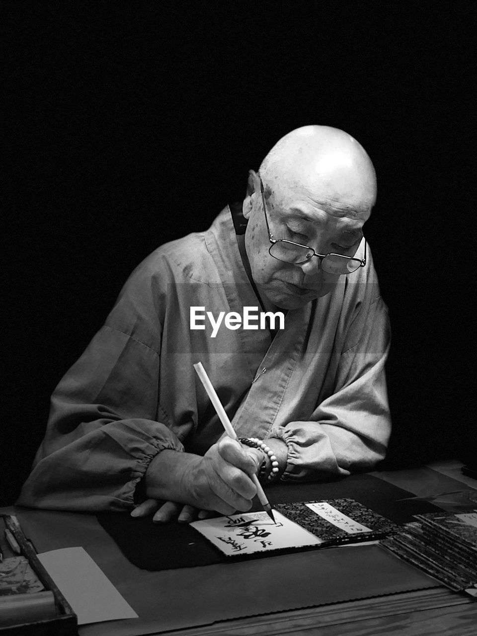 Senior man writing at table against black background