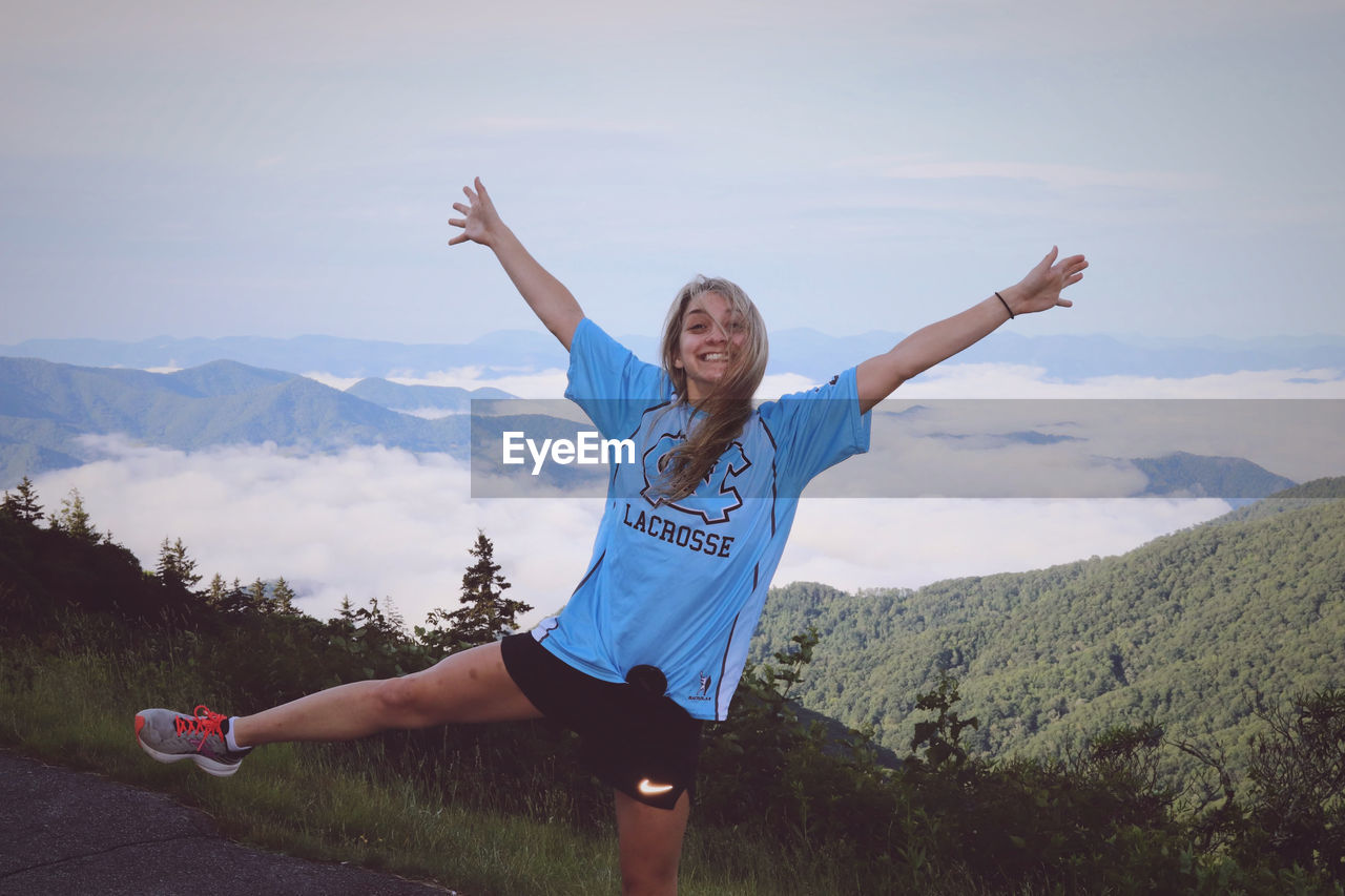 WOMAN WITH ARMS RAISED AGAINST MOUNTAIN RANGE