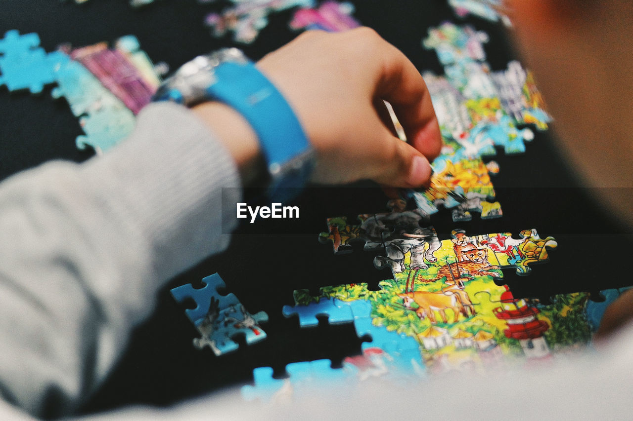 Cropped hand of boys holding jigsaw pieces