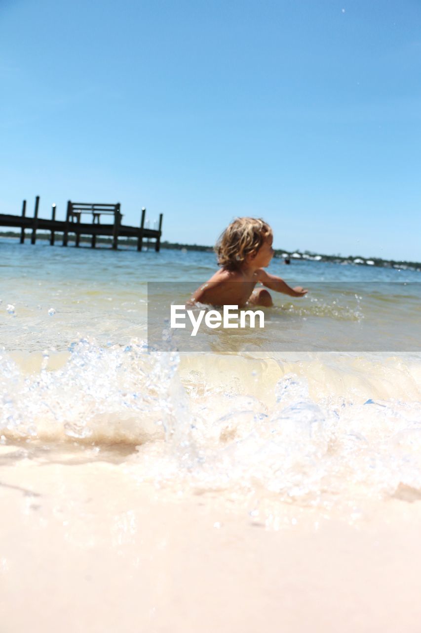 REAR VIEW OF SHIRTLESS BOY ON BEACH