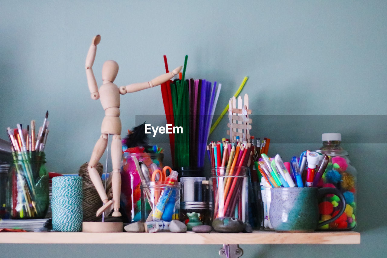 Close-up of multi colored pencil and figurine on shelf by wall