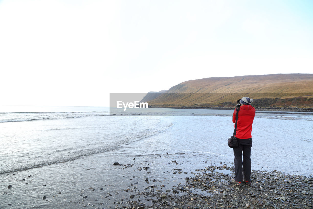 Rear view of woman photographing sea against clear sky