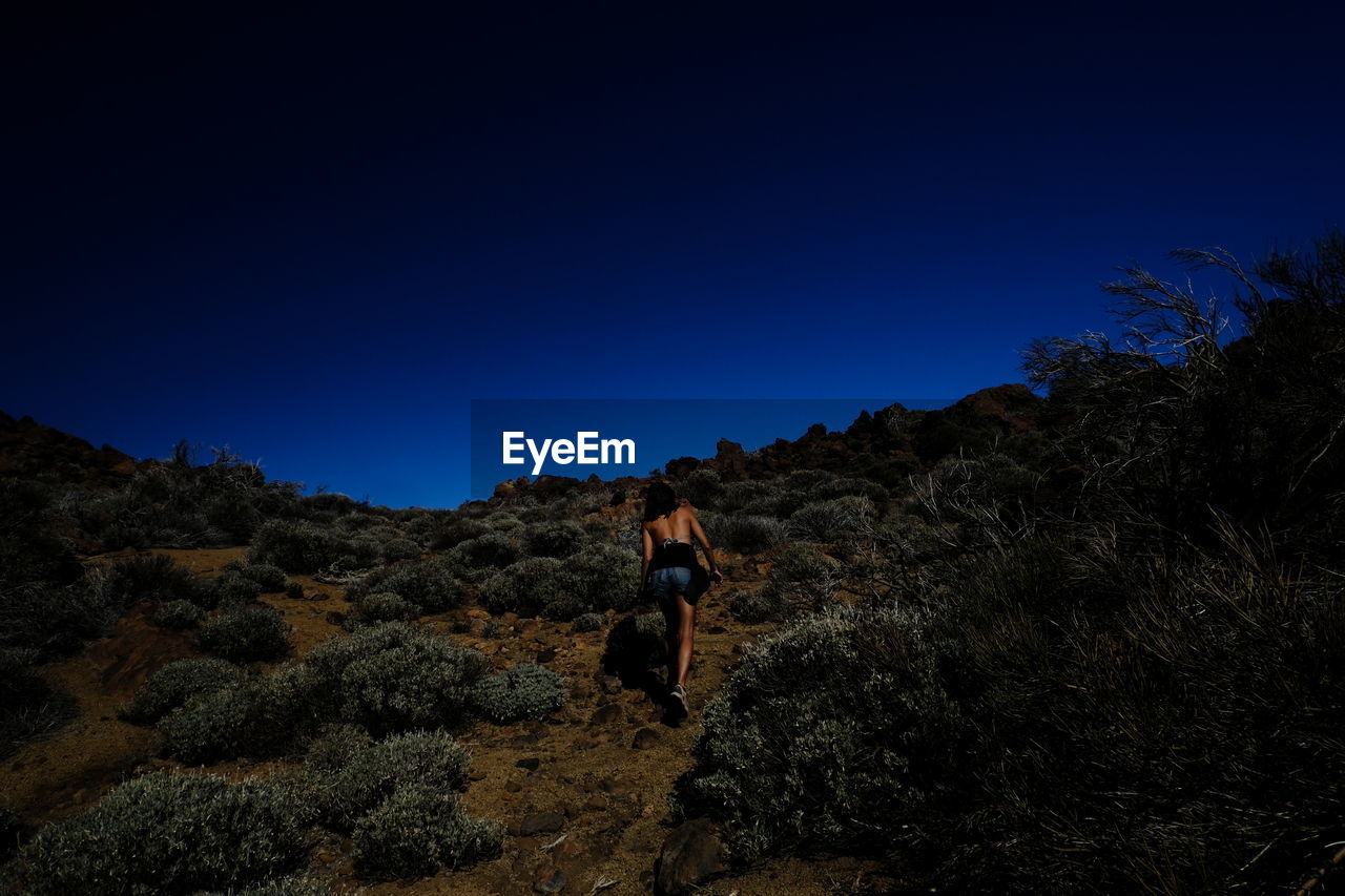 Woman standing on rock against blue sky