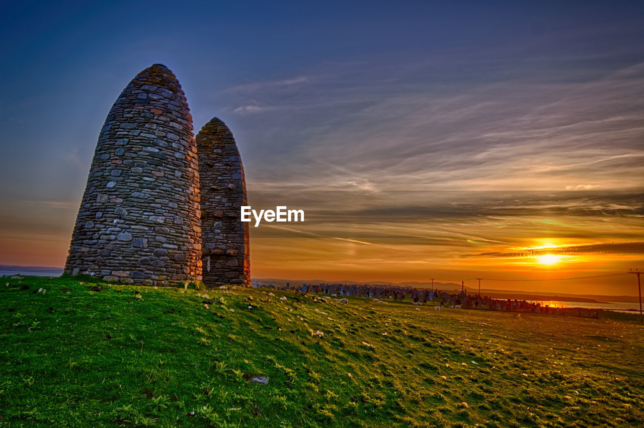 Stone wall on field against sky during sunset