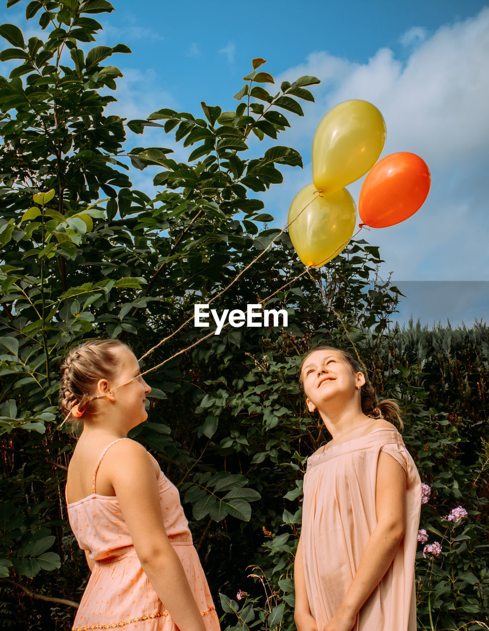 Portrait of a smiling girls with balloons against trees