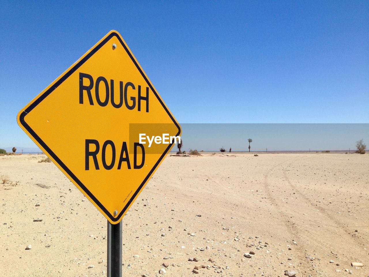 Road sign on barren landscape against clear blue sky