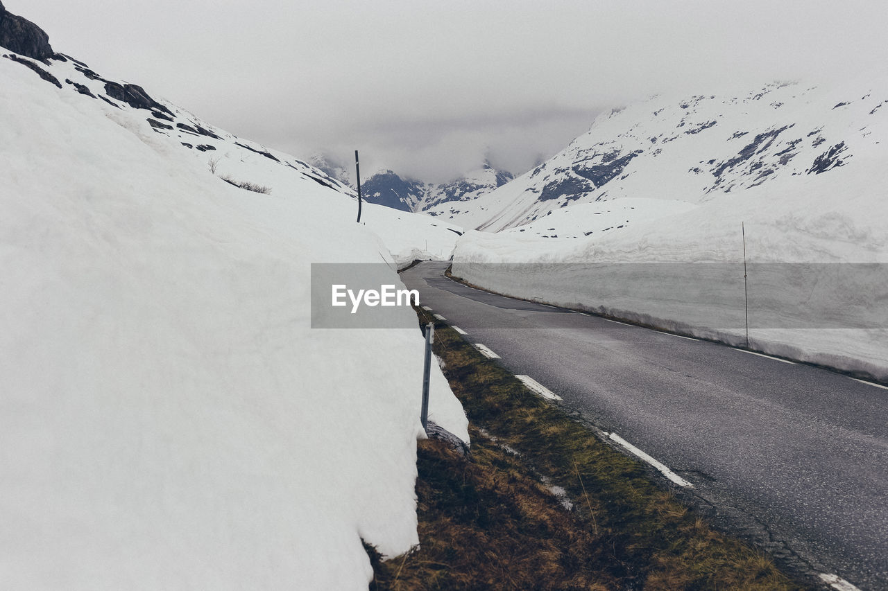 SNOW COVERED ROAD AGAINST MOUNTAIN