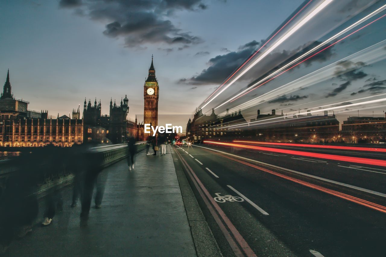 Light trails on road against big ben during sunset in city