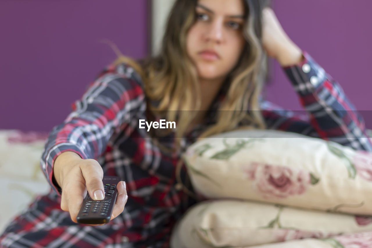 Attractive casual woman watching tv, switching channels with remote control in hand. 