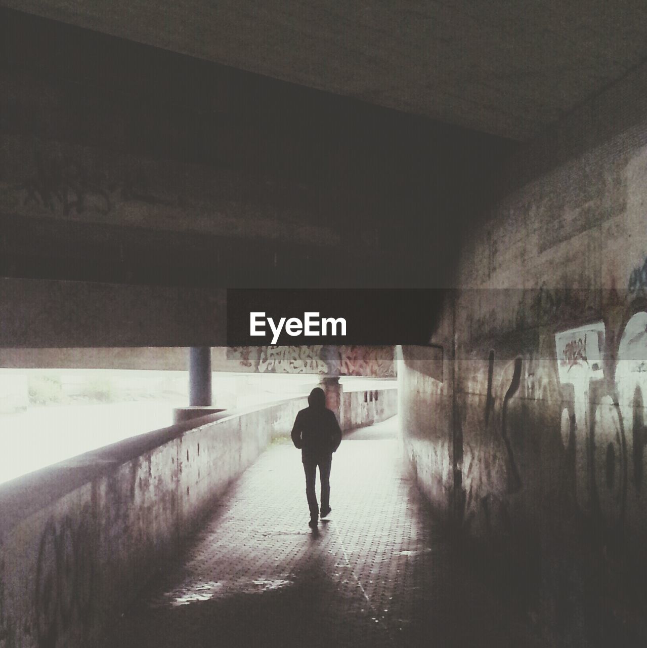 Silhouette of man walking under bridge