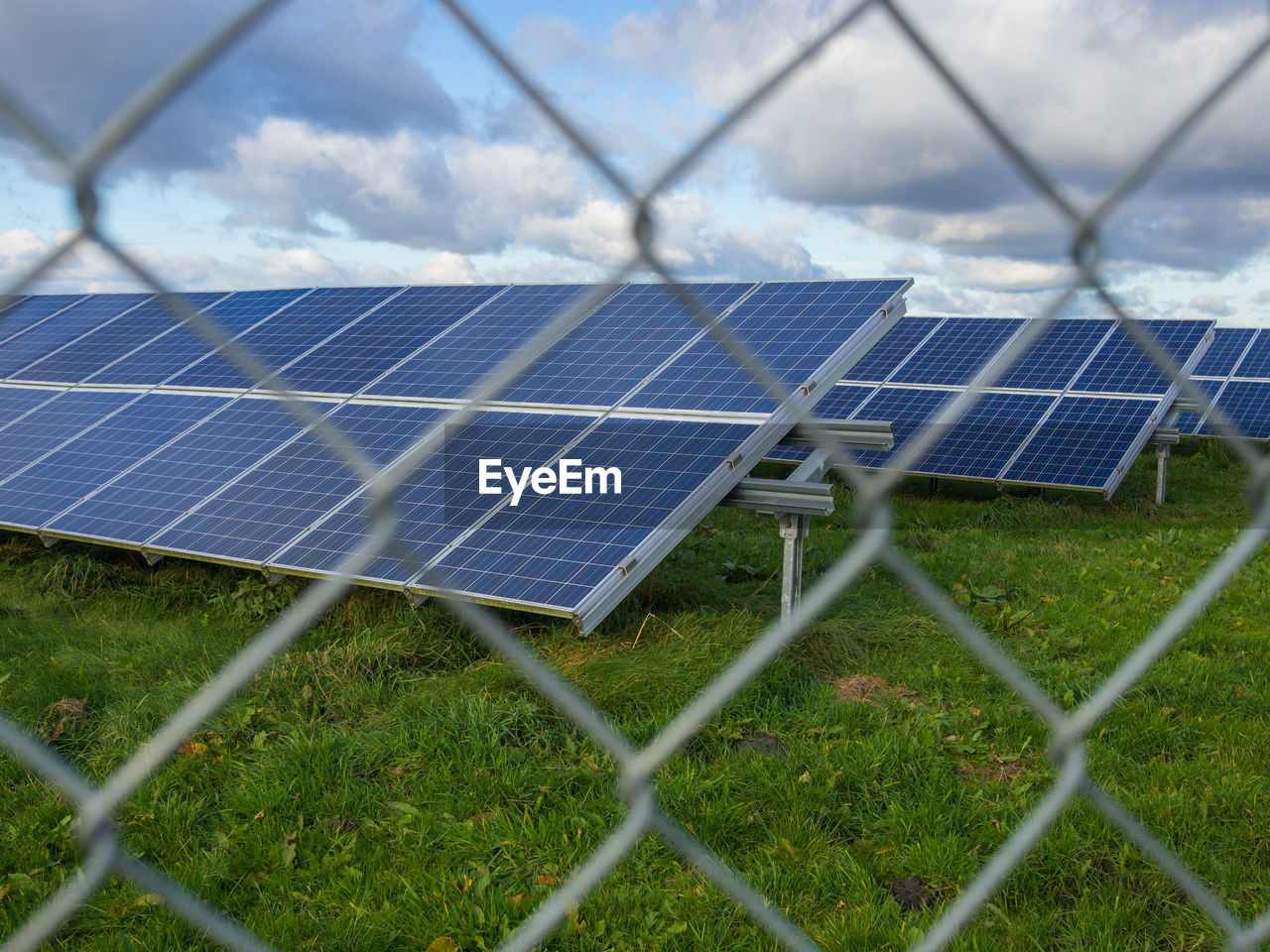 Low angle view of solar panel farm behind metal fence on field against sky, germany