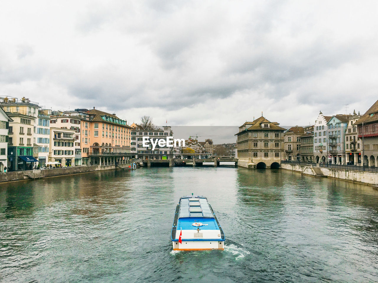 Boat on canal in city against cloudy sky