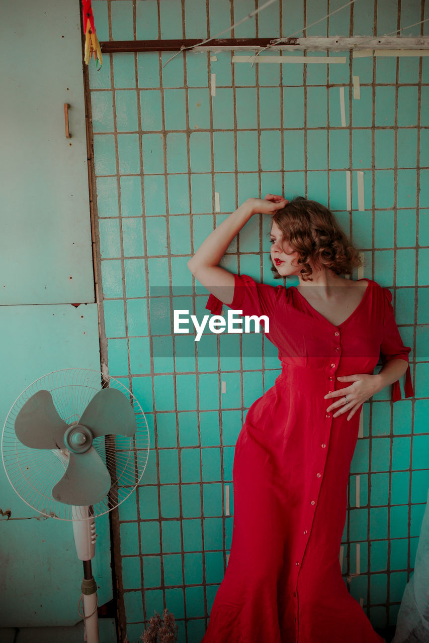 Woman standing by electric fan against wall